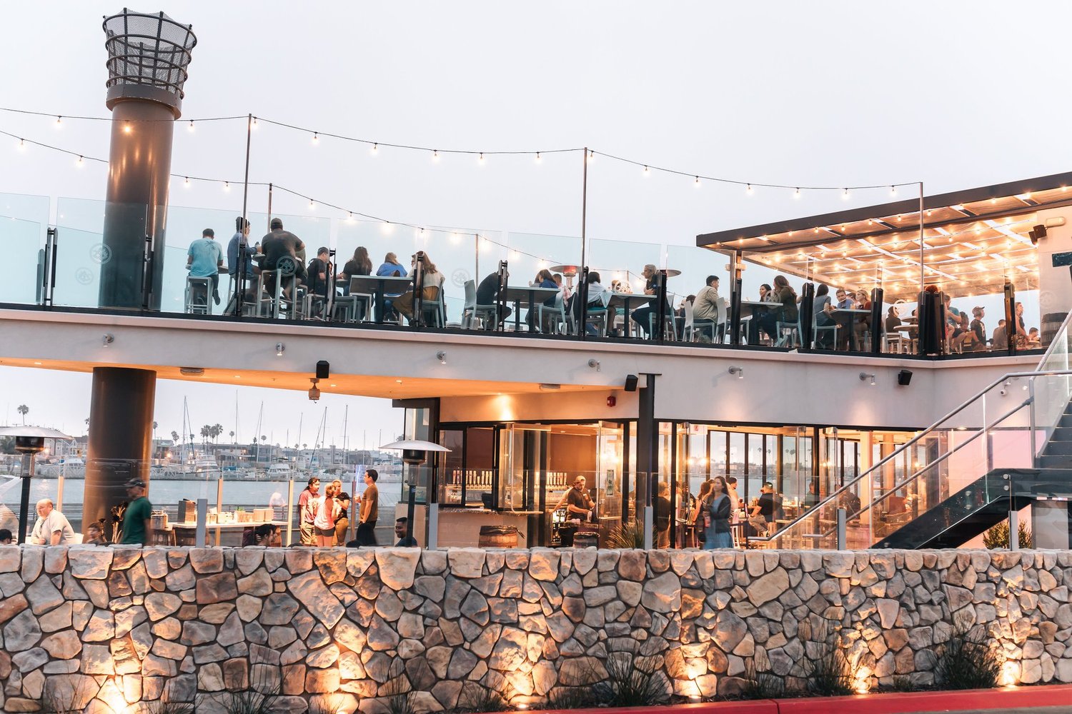 Ballast Point Brewery exterior at dusk - multi-level waterfront venue with string lights and marina views