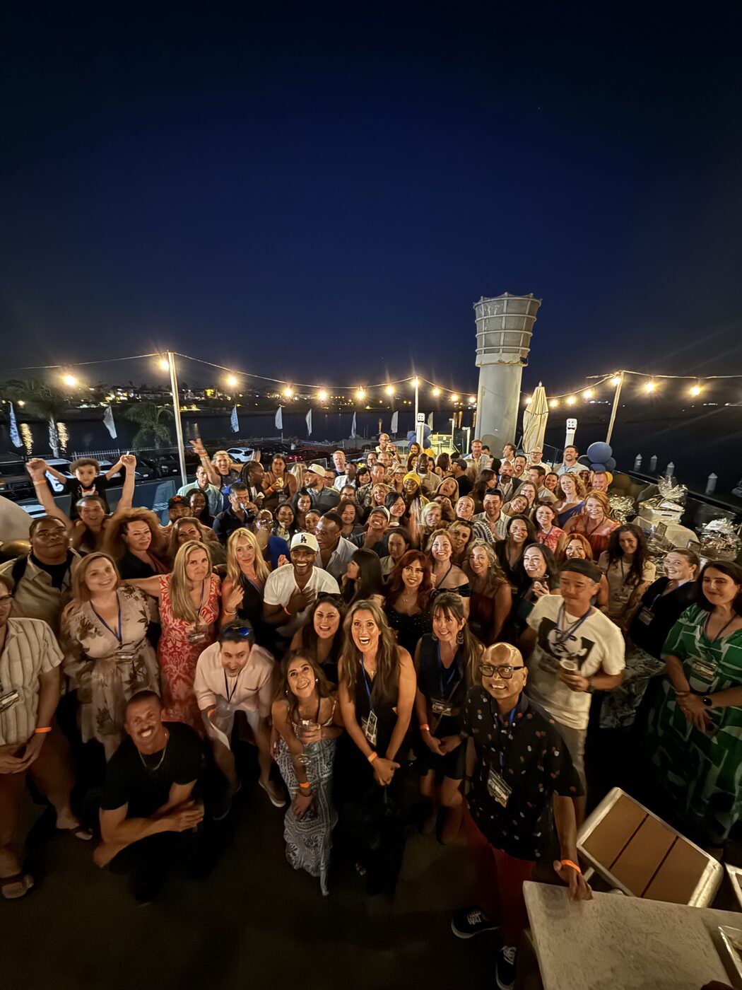 The Millikan Class of 2001 gathered on the waterfront deck at Ballast Point Brewery at night, under string lights